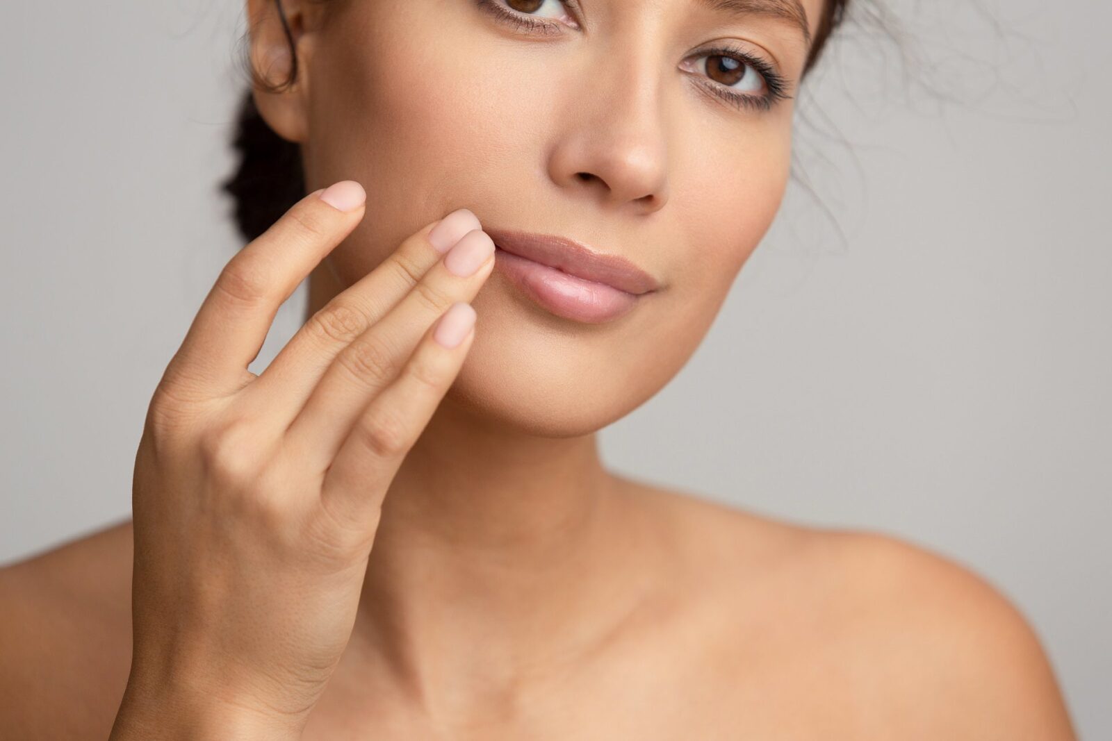 Natural beauty. Woman applying balsam, touching lips, grey studio background