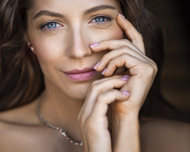 Close-up portrait of a 40 years old blue eyed woman. She touching her face and looking at camera. Sin care concept in the age after 40, How to achieve radiant skin