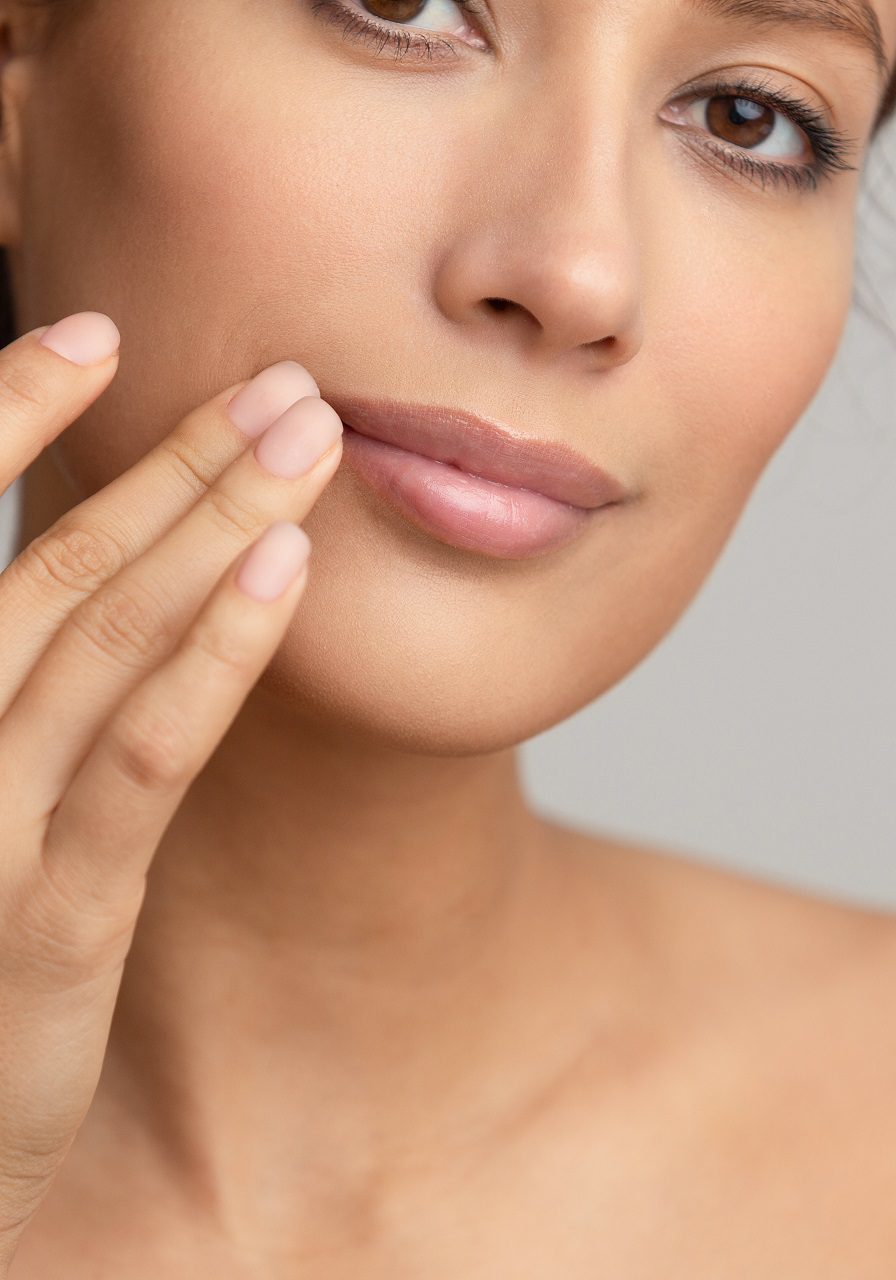 Natural beauty. Woman applying balsam, touching lips, grey studio background